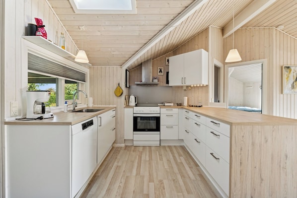 Moderni keittiö, jossa on valkoiset kaapit, sisäänrakennettu uuni ja ikkuna, josta avautuu näkymä vehreään maisemaan.
