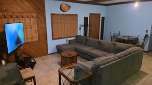 A living room with a sectional sofa, a glass coffee table, a television, and a ceiling fan. - Peaceful cabin near Grand Lake and Disney on big lot (Pensacola)