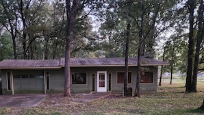 A single-story building with a garage, surrounded by trees and grassy area. - Peaceful cabin near Grand Lake and Disney on big lot (Pensacola)