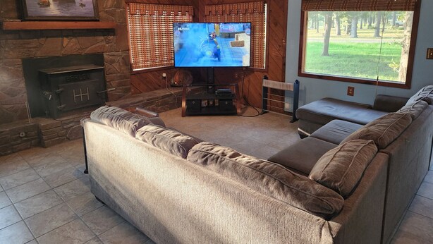 A living room with a fireplace, a large TV, and a view of a park. - Peaceful cabin near Grand Lake and Disney on big lot (Pensacola)