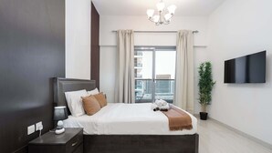 Un dormitorio moderno con una cama grande, una mesita de noche, un televisor montado en la pared y una planta en maceta.