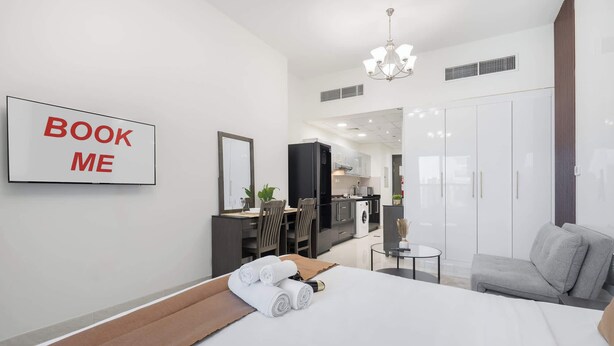 Una habitación de hotel moderna con cama, escritorio, espejo, armario y kitchenette.
