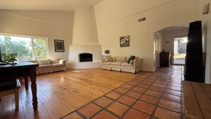 A spacious living room with a fireplace, two sofas, a wooden coffee table, and a large window. - 3-bedroom house with Pool, Sauna in Ojai (Ojai)