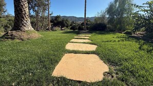 A pathway leading through a well-maintained grassy area with palm trees and a clear view of distant hills. - 3-bedroom house with Pool, Sauna in Ojai (Ojai)