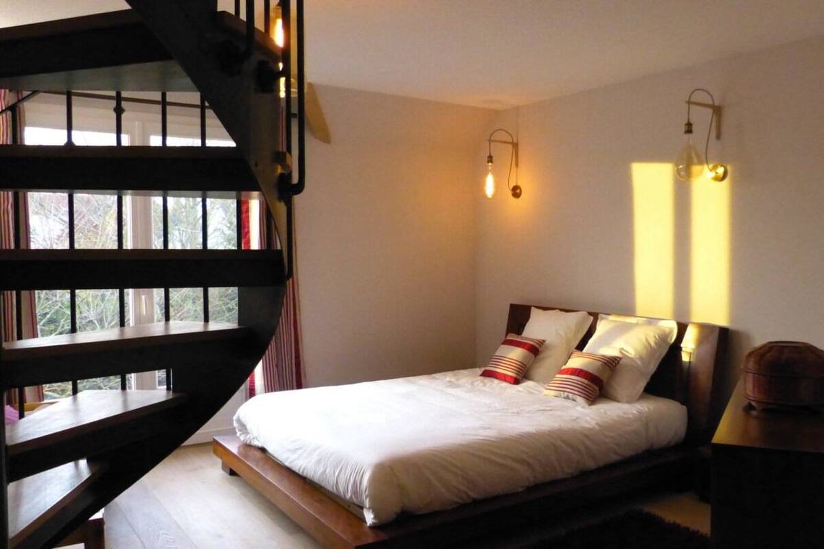 Une chambre à coucher avec un lit, une table de chevet, une lampe et une fenêtre avec des rideaux.