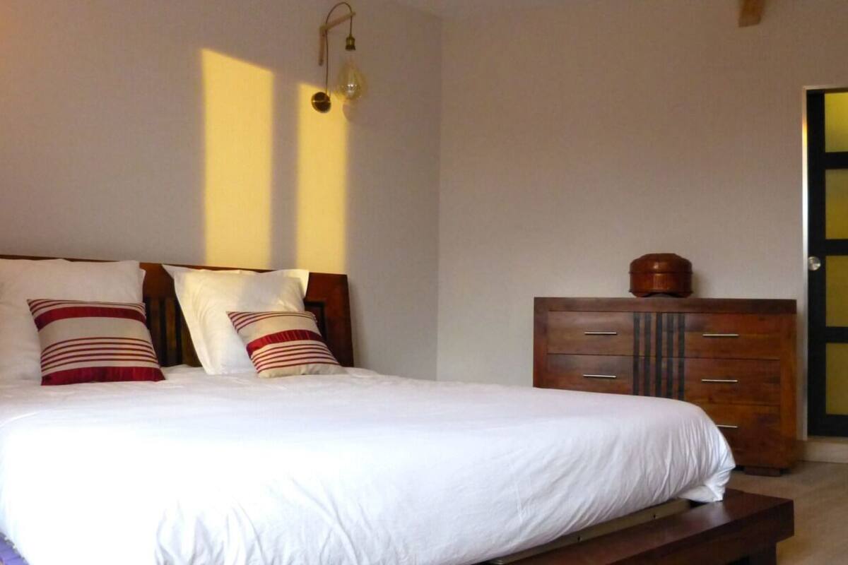 Une chambre à coucher avec un grand lit, une commode en bois et une porte dont les panneaux sont en verre dépoli.