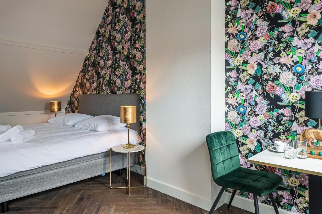 Ein Hotelzimmer mit einem Bett, Nachttischlampen, einem kleinen Tisch mit Stuhl und Blumenmuster-Tapete.