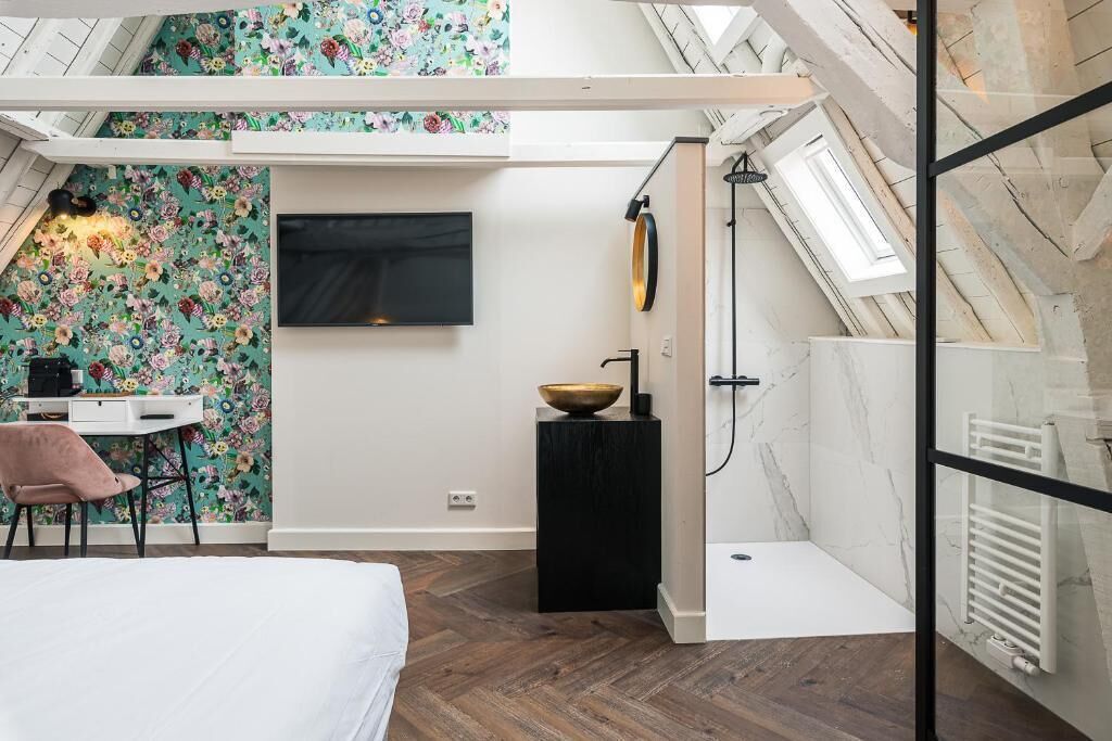 Een slaapkamer met dakraam, een bed, een bureau met stoel, een televisie en een badkamer met douche.