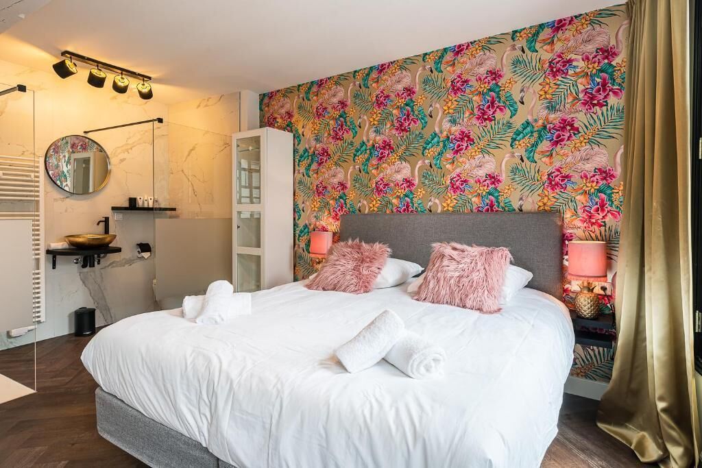 A modern bedroom with a large bed, a mirror, a vanity, and a floral-patterned wall.