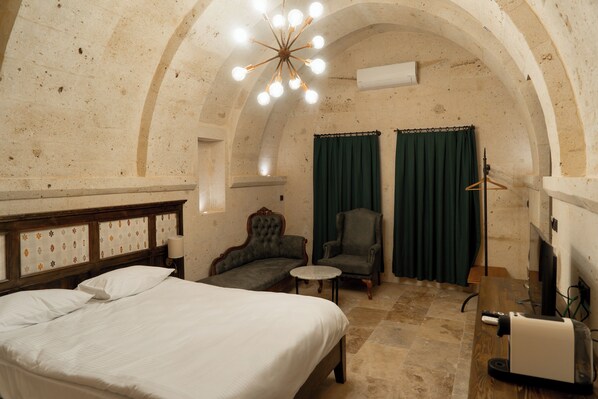 A room with a bed, a chair, a small table, and a desk with a computer. - Asra Cave Hotel (Nevşehir)