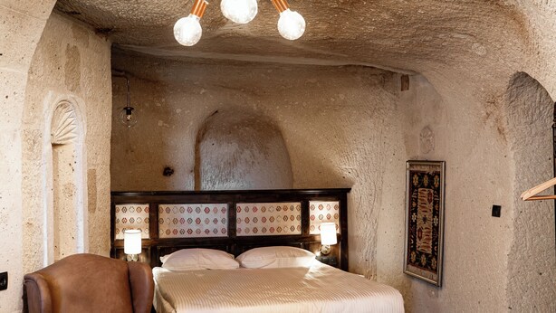 Ein Schlafzimmer mit Steindecke, einem hölzernen Bett, einem Ledersessel und einer Chandelier.