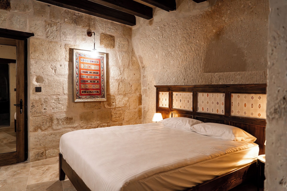 Un dormitorio con una cama grande, paredes de piedra, un cabecero de madera y un tapiz enmarcado en la pared.