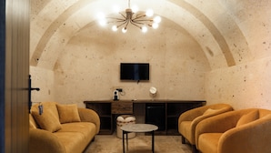 Ein gemütliches Wohnzimmer mit einer Couch, Sesseln, einem Couchtisch und einem an der Wand befestigten Fernseher.