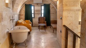 Ein Badezimmer mit einer Badewanne, zwei Sesseln, einem Sofa und einem Fenster mit Vorhängen.