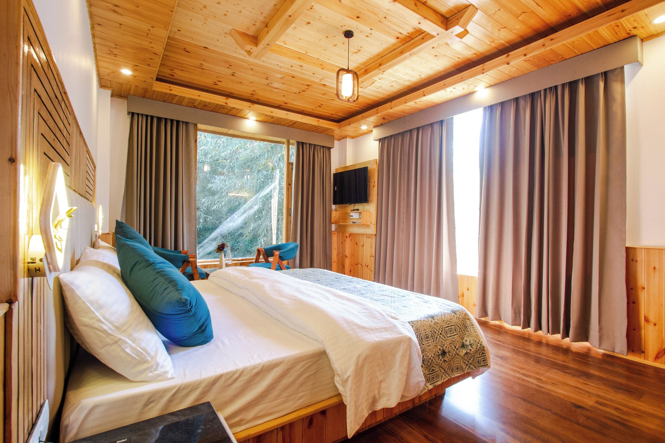 A wooden-paneled bedroom with a bed, curtains, a television, and a window.