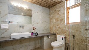 Un baño con pared de mármol, un lavamanos con artículos de aseo, un inodoro y una ducha.