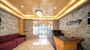 Un hall con pared de piedra, mostrador de recepción de madera, sofá rojo y una araña.