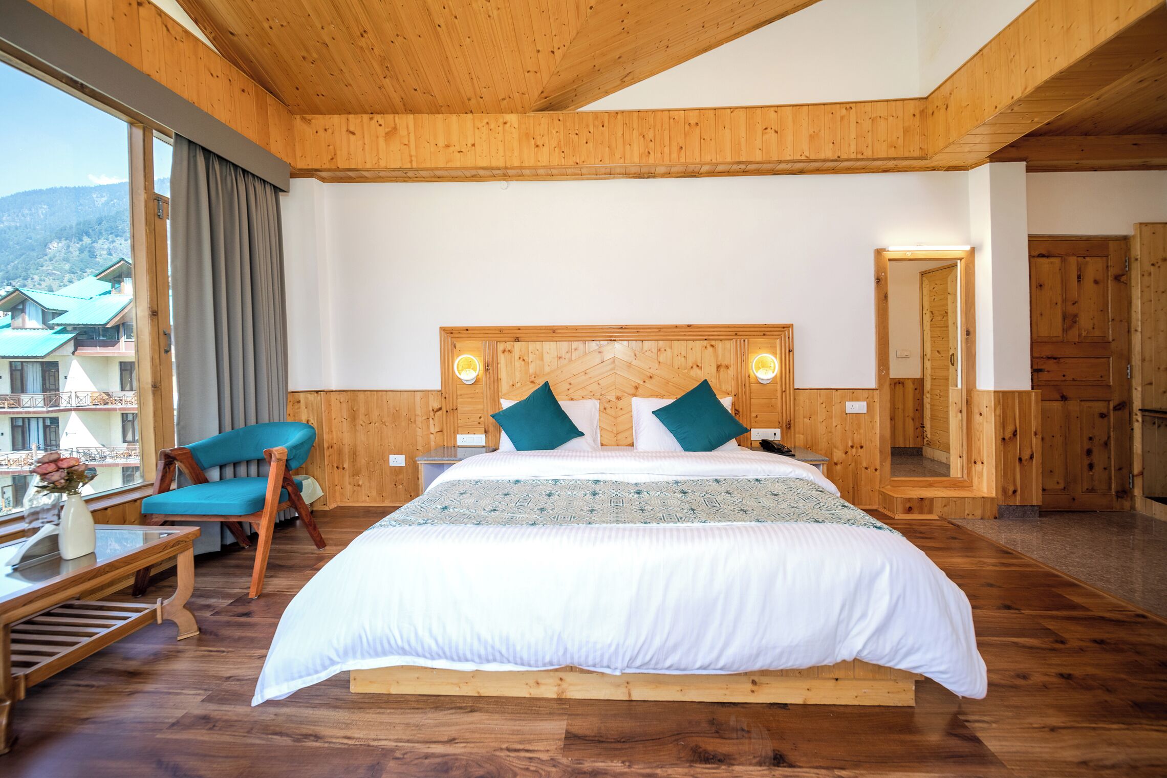 Un dormitorio con paneles de madera, una cama grande, una silla y vistas a edificios.