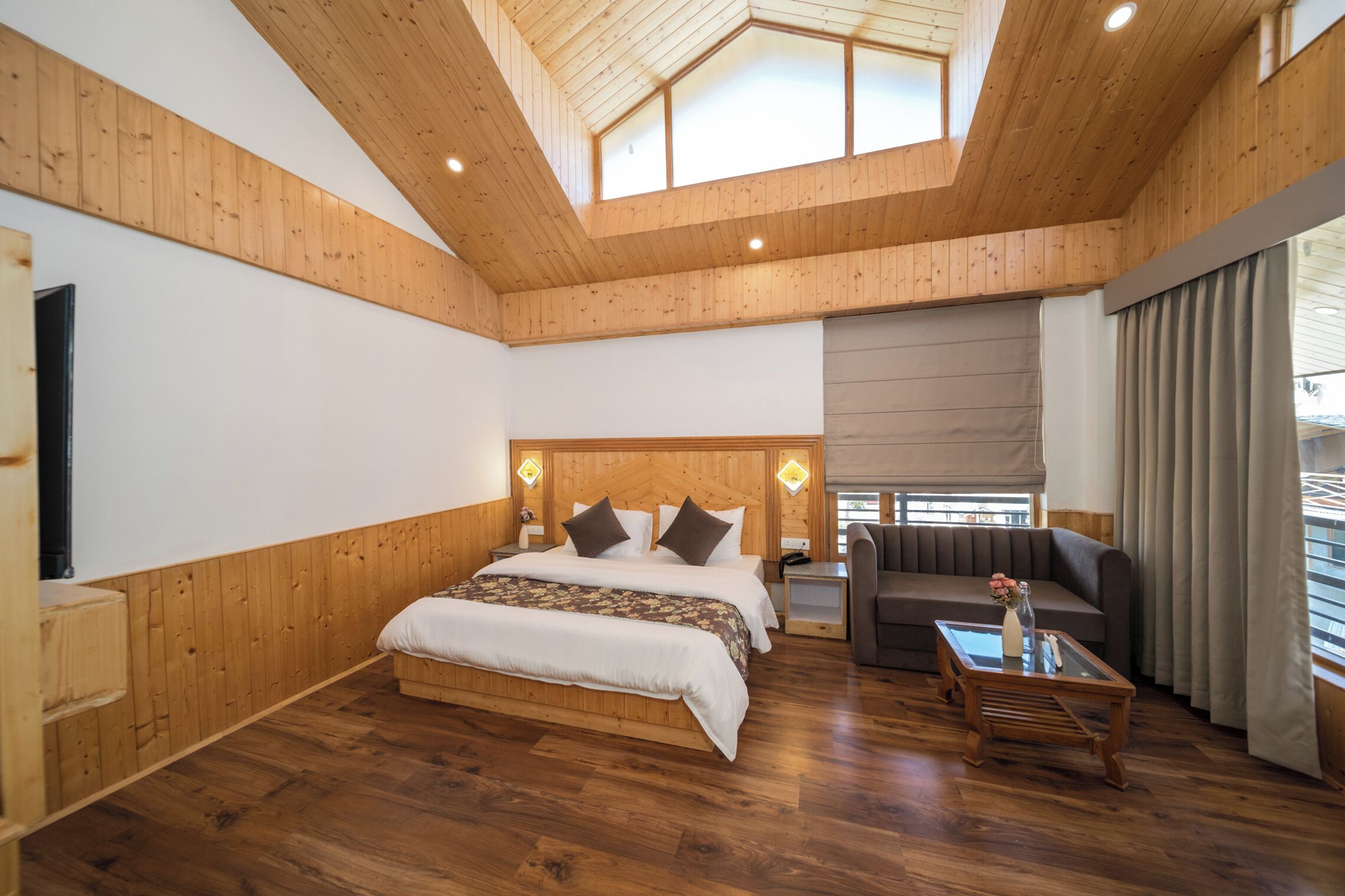 Een ruime kamer met een houten plafond, een groot bed met hoofdeinde, een bank en een salontafel.