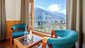 Una habitación con dos sillas color turquesa, una mesa de madera y un ventanal con vistas a la montaña.