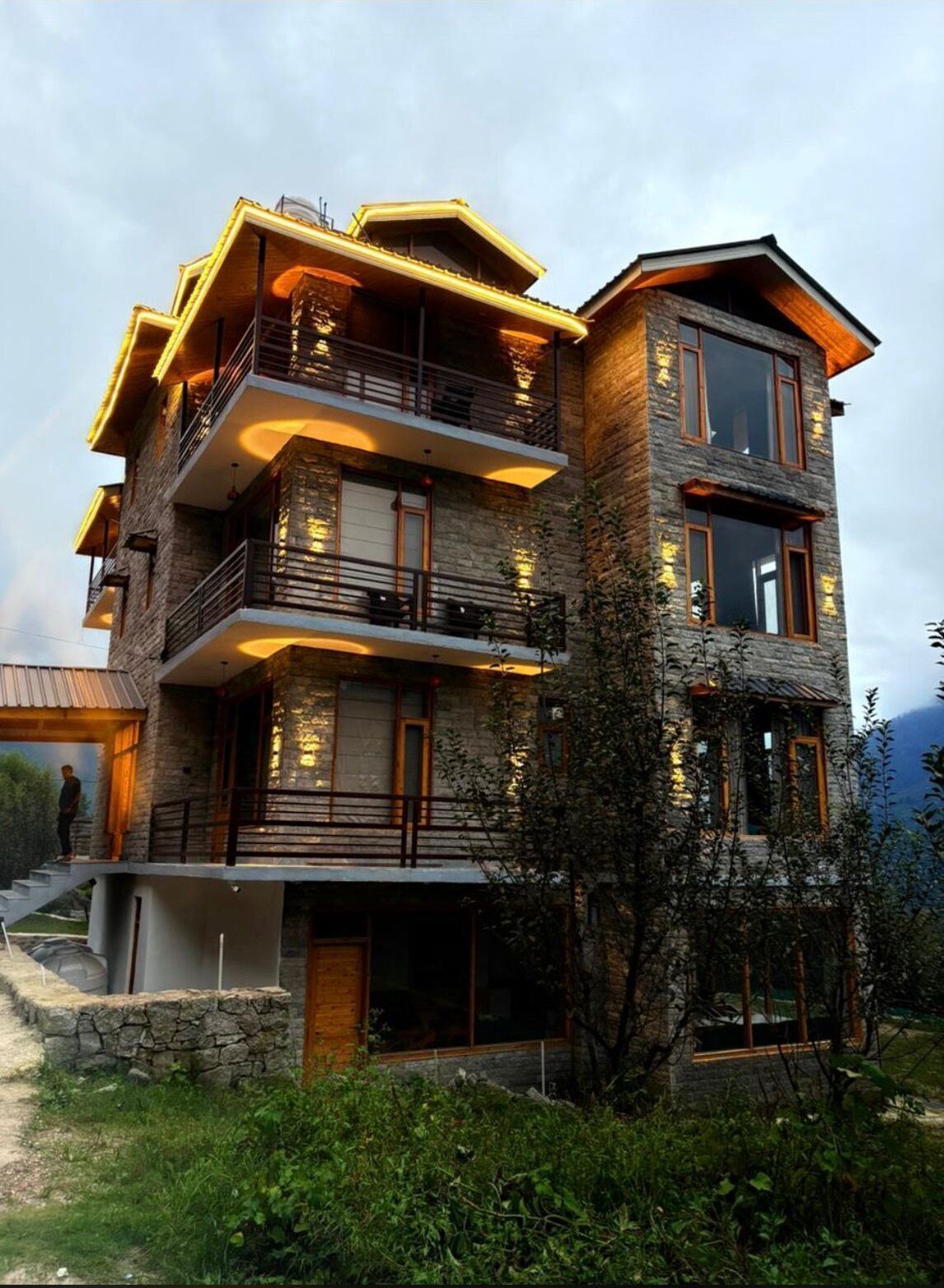 A multi-story stone building with balconies and large windows, surrounded by greenery.