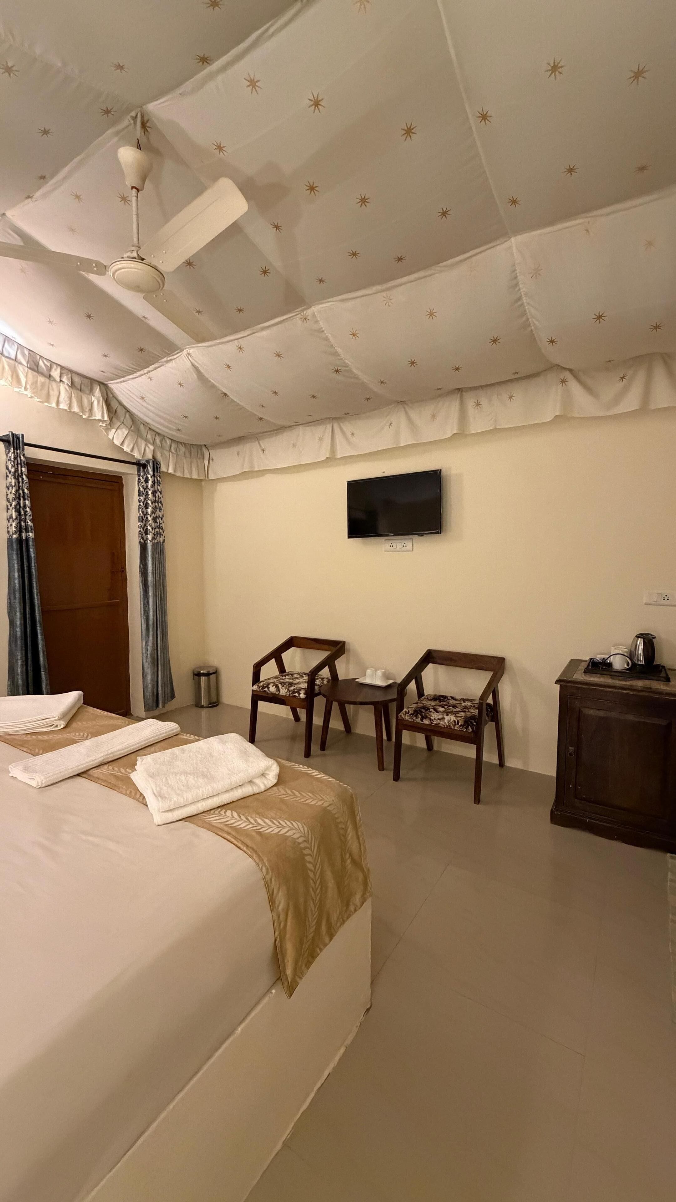 A hotel room with a bed, two chairs, a small table, a TV, and a nightstand.