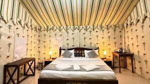 Una habitación con techo a rayas, una cama con cabecera decorada con un mosaico, dos mesitas de noche con lámparas y una pared con motivos de camellos y palmeras.