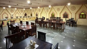 Un amplio comedor con varias mesas y sillas, un techo alto con diseño decorativo y suelo de baldosas.