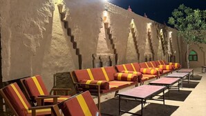 Un área de estar al aire libre con sillones reclinables y mesas, un muro de piedra con escalones y un cielo nocturno.