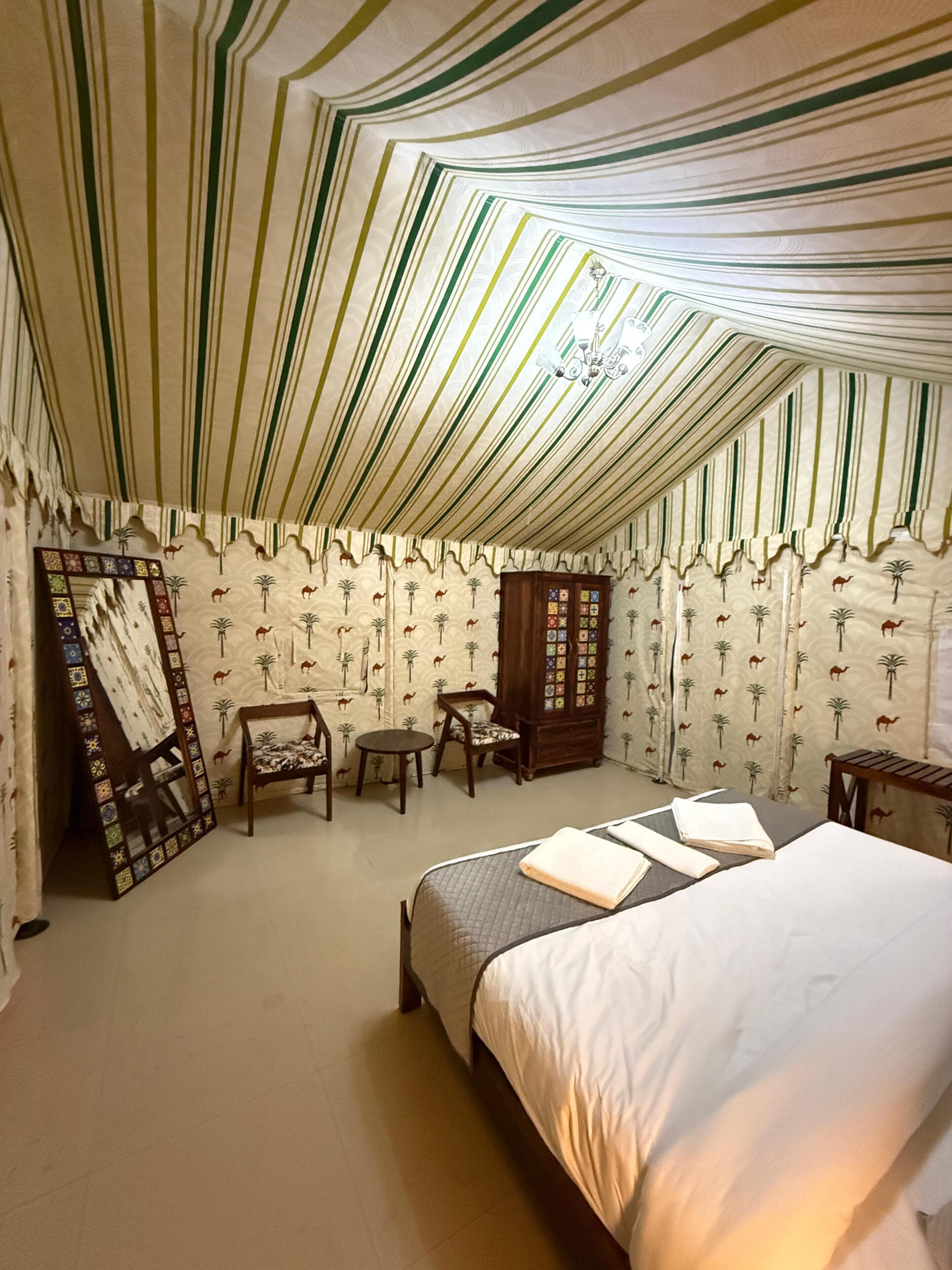 A tented room with a bed, a small table, a chair, and a cabinet.