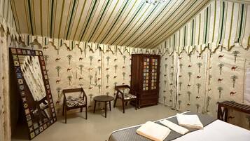 A tented room with a bed, a small table, a chair, and a cabinet.