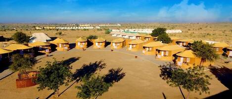 Ein Wüstenresort mit in Halbkreis angeordneten Jurten, umgeben von vereinzelter Vegetation und einem klaren Himmel.