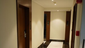 Un couloir doté d’un sol en marbre, de portes en bois et d’un plafond pourvu d’un éclairage encastré.