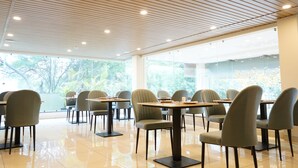 Un espace repas moderne, doté de tables et de chaises, de grandes fenêtres et d’un plafond en bois.