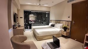 Une chambre d’hôtel moderne équipée d’un lit, d’un bureau avec un ordinateur portable, d’une chaise et d’une salle de bain visible à travers une porte en verre.