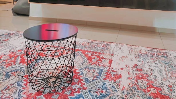 Een moderne woonkamer met een grote flatscreen televisie aan een houten wand, een zwarte salontafel en een kamerbreed tapijt met een patroon.