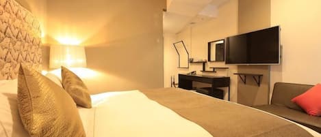 Una habitación de hotel con cama, escritorio, televisor y sofá.
