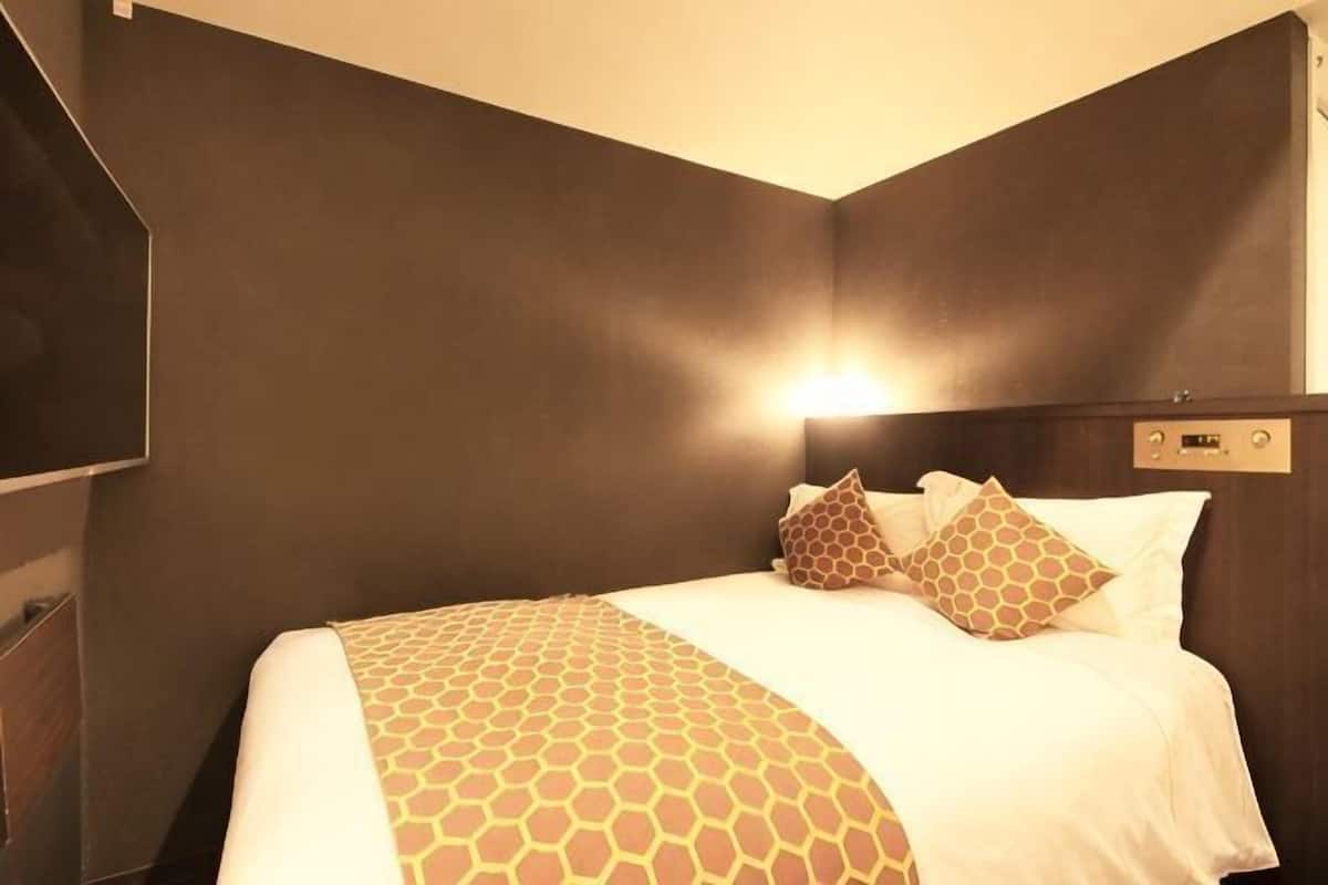 A hotel room with a large bed, a headboard with controls, and a wall-mounted TV.