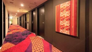 Un pasillo de hotel con alfombra estampada, paredes oscuras y una obra de arte grande a la derecha.
