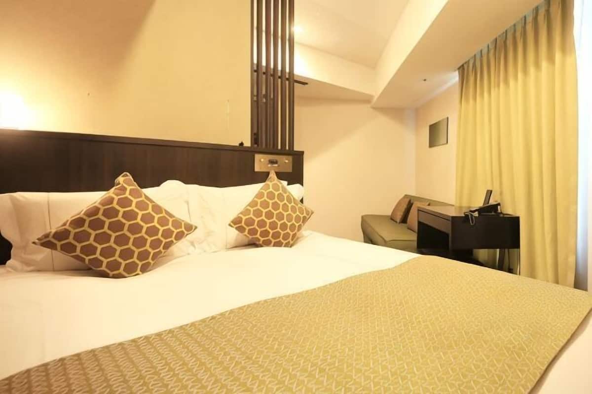 A hotel room with a large bed, a desk, a chair, and a lamp.
