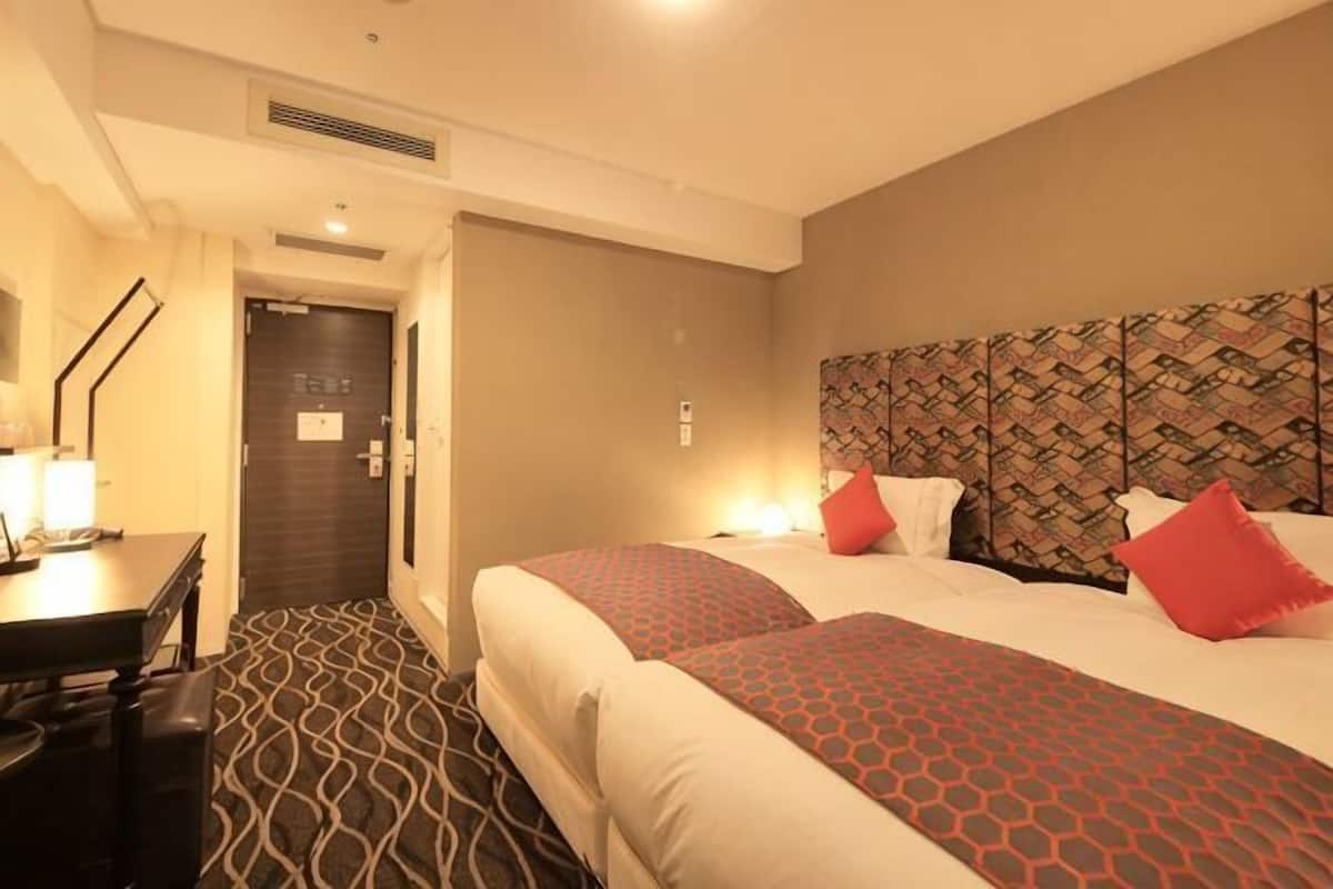 A hotel room with two beds, a desk, and a door.