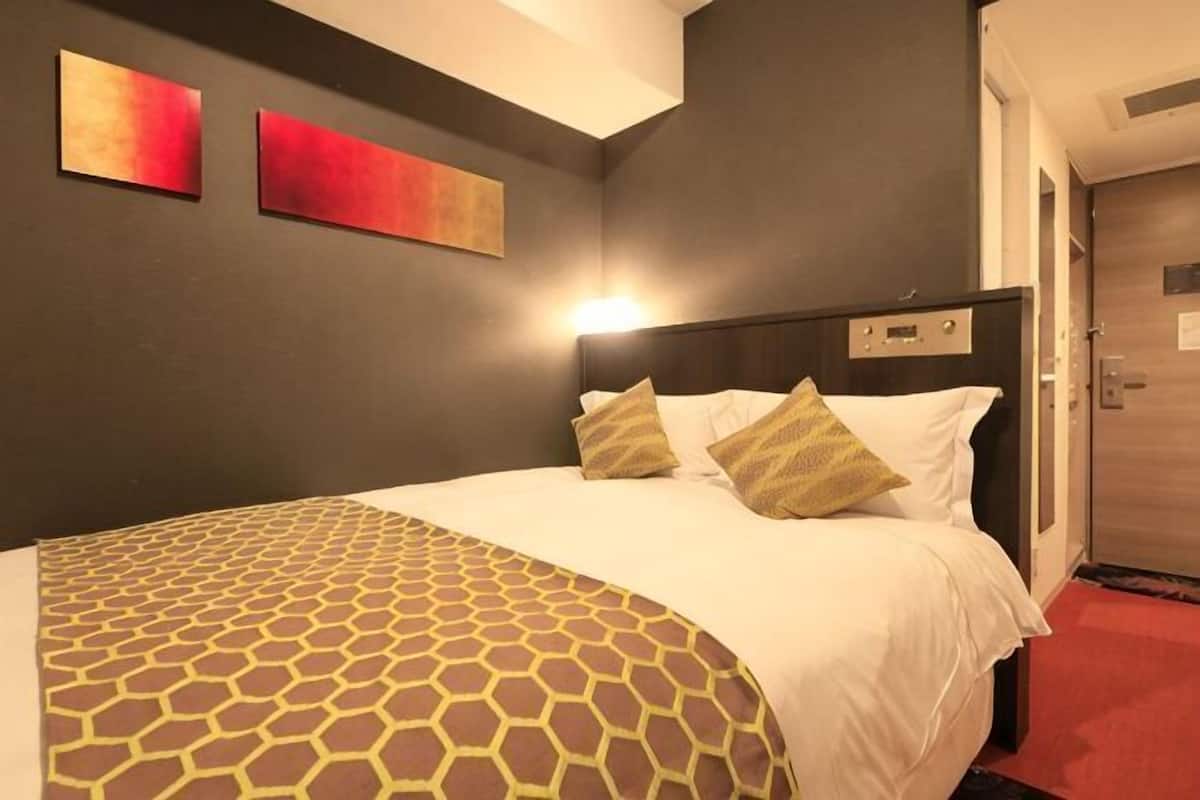 A hotel room with a bed, a headboard, and a wall with two paintings.
