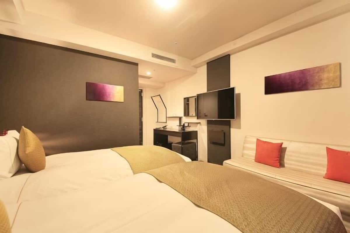 A hotel room with a bed, bedside table, TV, and artwork on the walls.