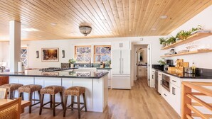 Une cuisine moderne dotée d’un îlot central, de tabourets de bar, d’un plancher en bois et d’appareils électroménagers intégrés.