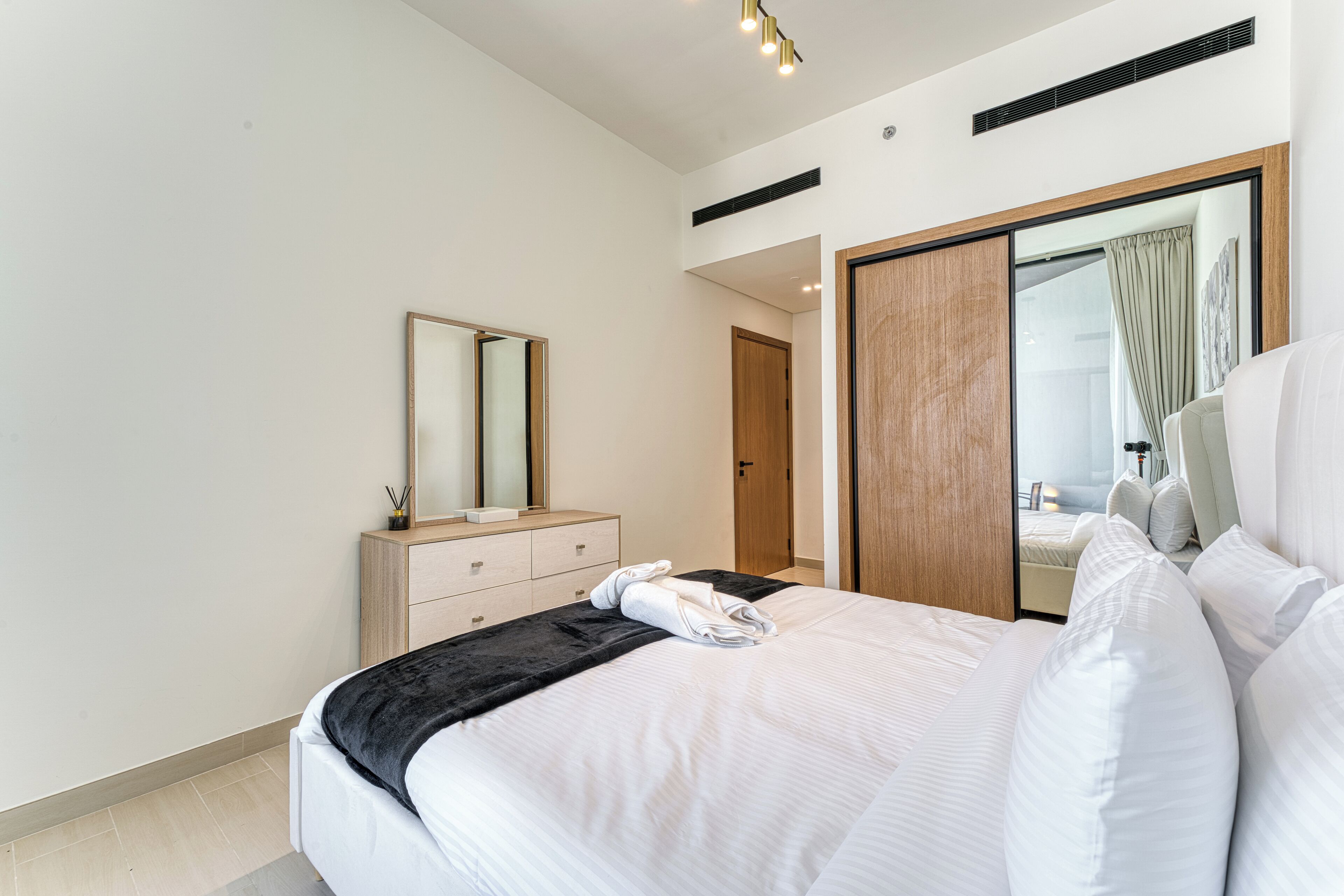 Moderni hotellihuone, jossa on suuri sänky, puinen vaatekaappi, peili ja liukuovi, joka johtaa parvekkeelle.