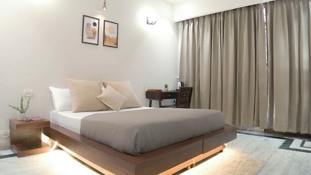 A modern bedroom with a wooden platform bed, a bedside table with a lamp, a small plant, and a nightstand.