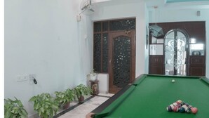 A room with a green pool table, a door with a decorative glass panel, and several potted plants along the wall.