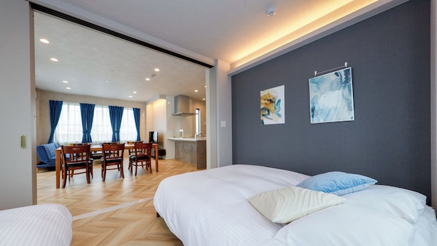 Une chambre d’hôtel moderne avec un grand lit, un coin repas avec des chaises et une cuisine en arrière-plan.