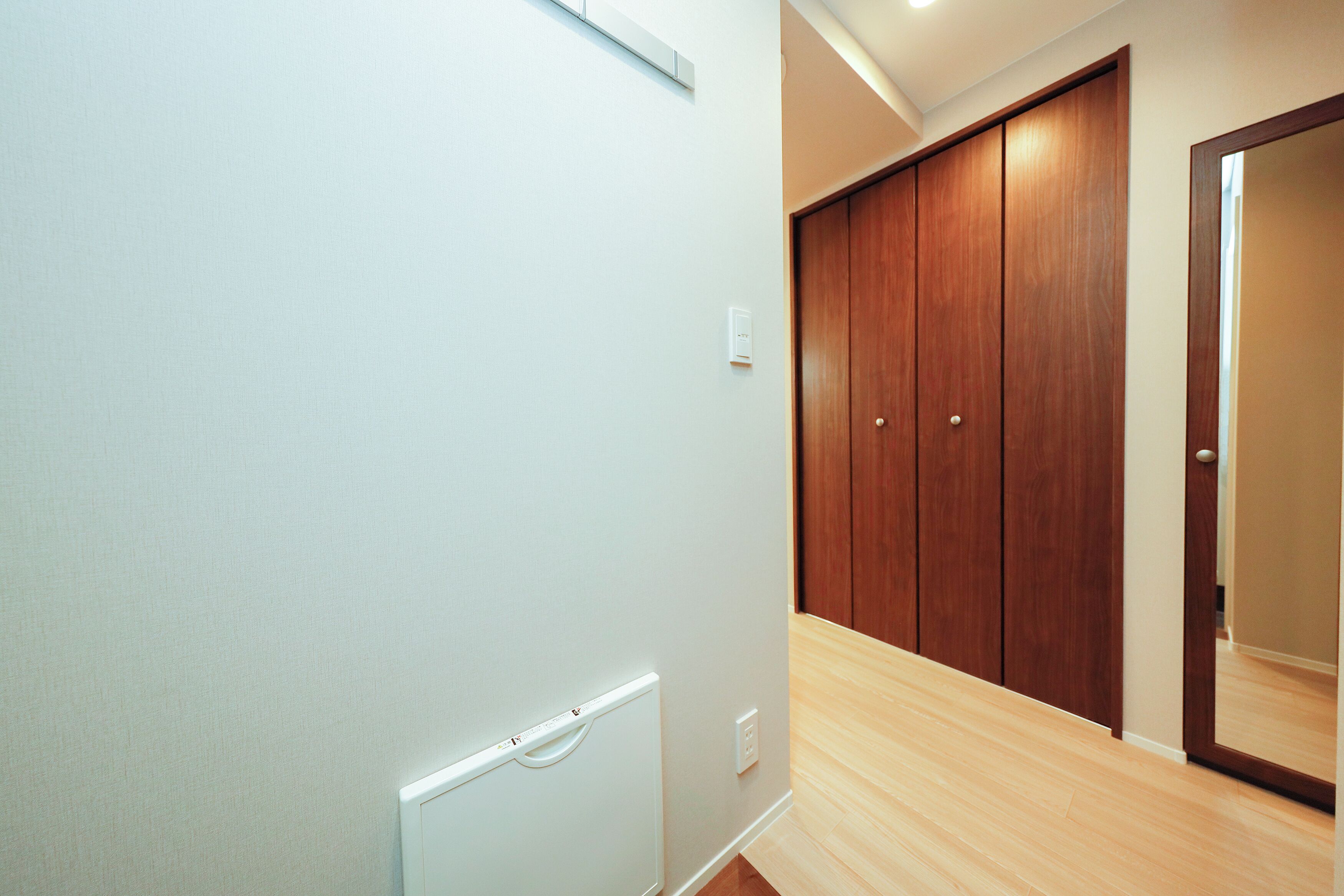 A hallway with a wooden wardrobe, a white wall, and a light switch.