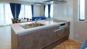 Une cuisine moderne dotée d’un grand îlot central, d’appareils électroménagers en acier inoxydable et d’un coin repas agrémenté de rideaux bleus.